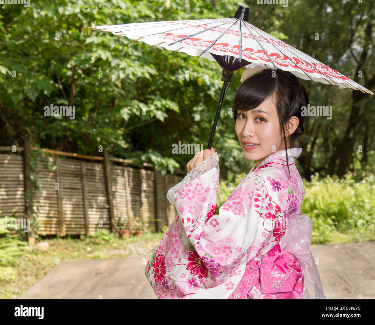 Femme Asiatique dans un kimono dans un jardin de style japonais tenant un parapluie Banque D'Images