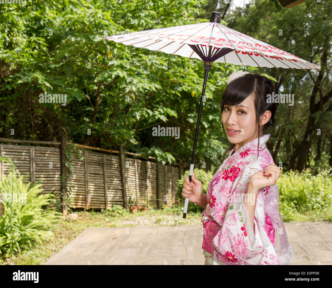 Femme Asiatique dans un kimono dans un jardin de style japonais tenant un parapluie Banque D'Images