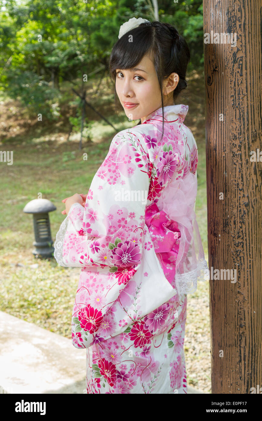 Femme Asiatique dans un kimono dans un jardin de style japonais appuyé contre le pilier Banque D'Images