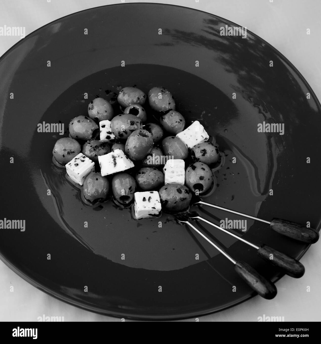 Droit - Olives avec de l'huile, les herbes, le fromage feta et les brochettes sur une plaque Banque D'Images