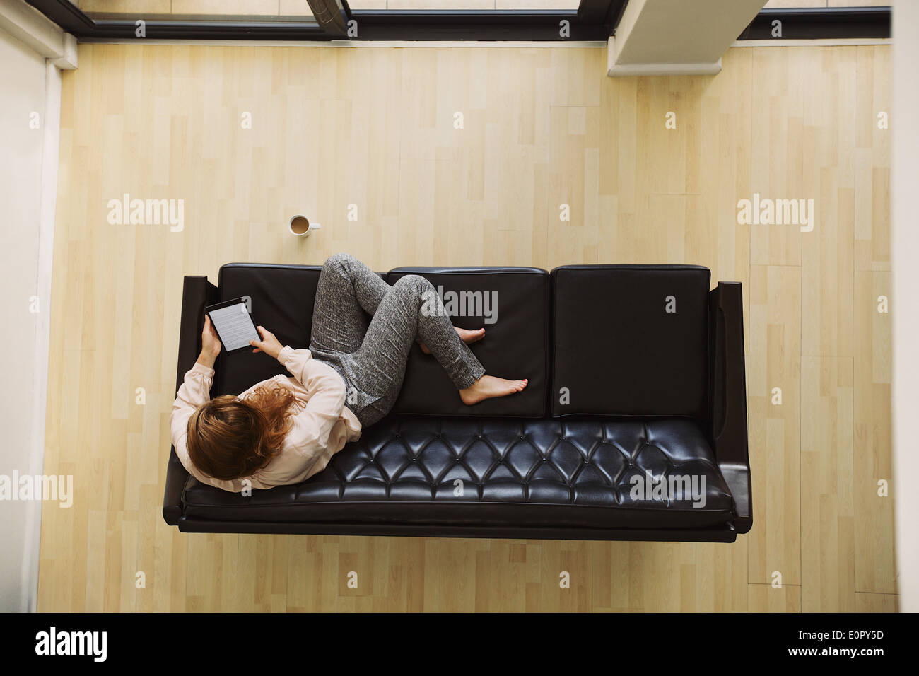Vue de dessus de jeune femme assise sur une table à l'aide de la tablette numérique. Female relaxing on sofa avec un e-reader dans son appartement. Banque D'Images