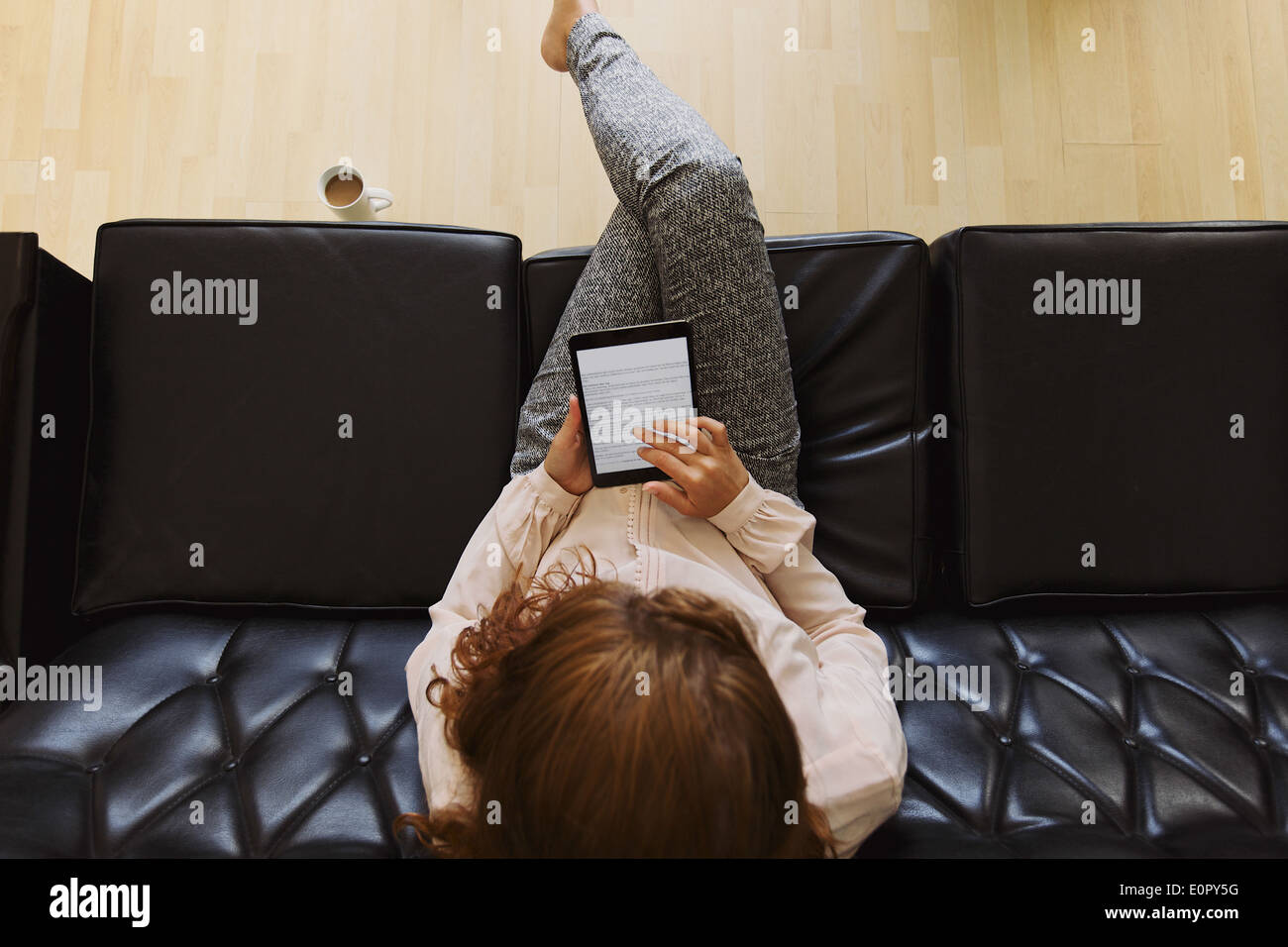 Top View of young brunette using digital tablet while sitting on a couch. Femme lisant un livre Banque D'Images