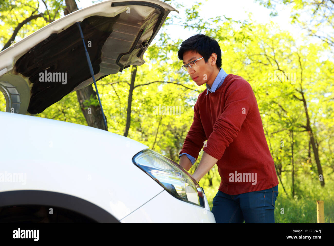 Vue latérale du portrait d'un jeune homme asiatique contrôler son moteur de voiture Banque D'Images