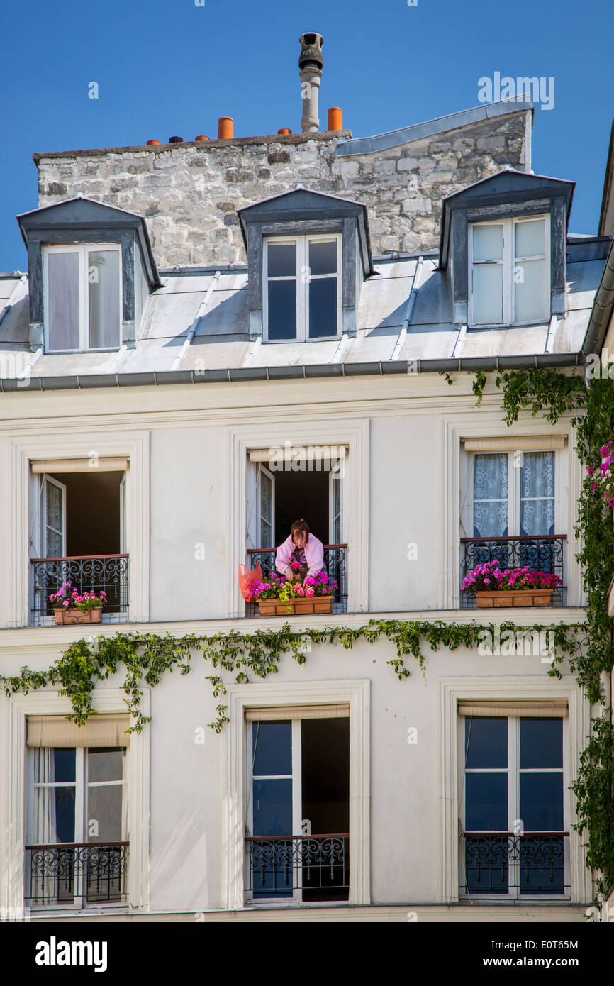 Femme sur la fenêtre géraniums fraisage balcon de son appartement dans le quartier du Marais à Paris France Banque D'Images
