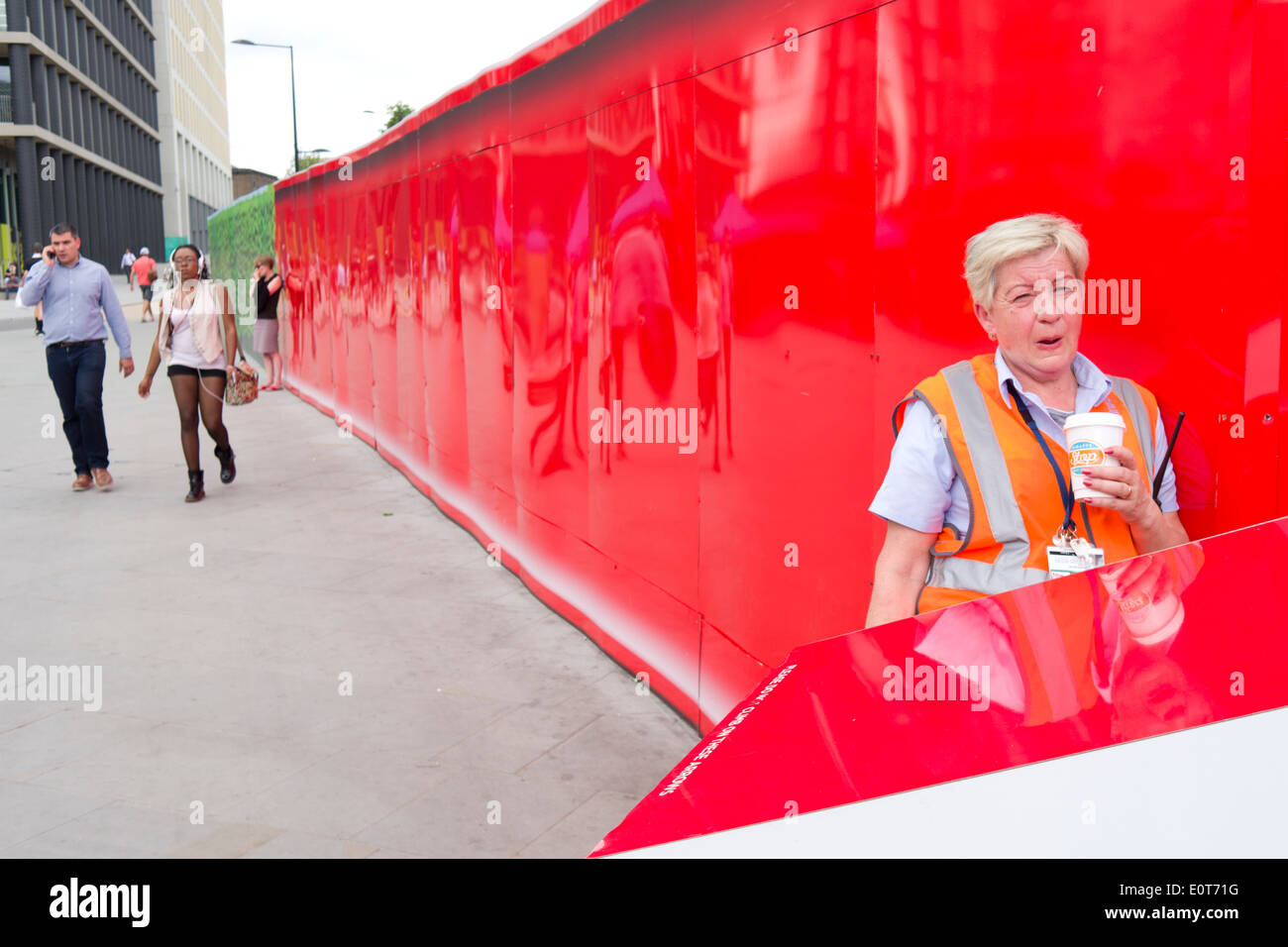 Un travailleur féminin se dresse contre un mur rouge, ayant une pause-café à King's Cross, Londres. Banque D'Images