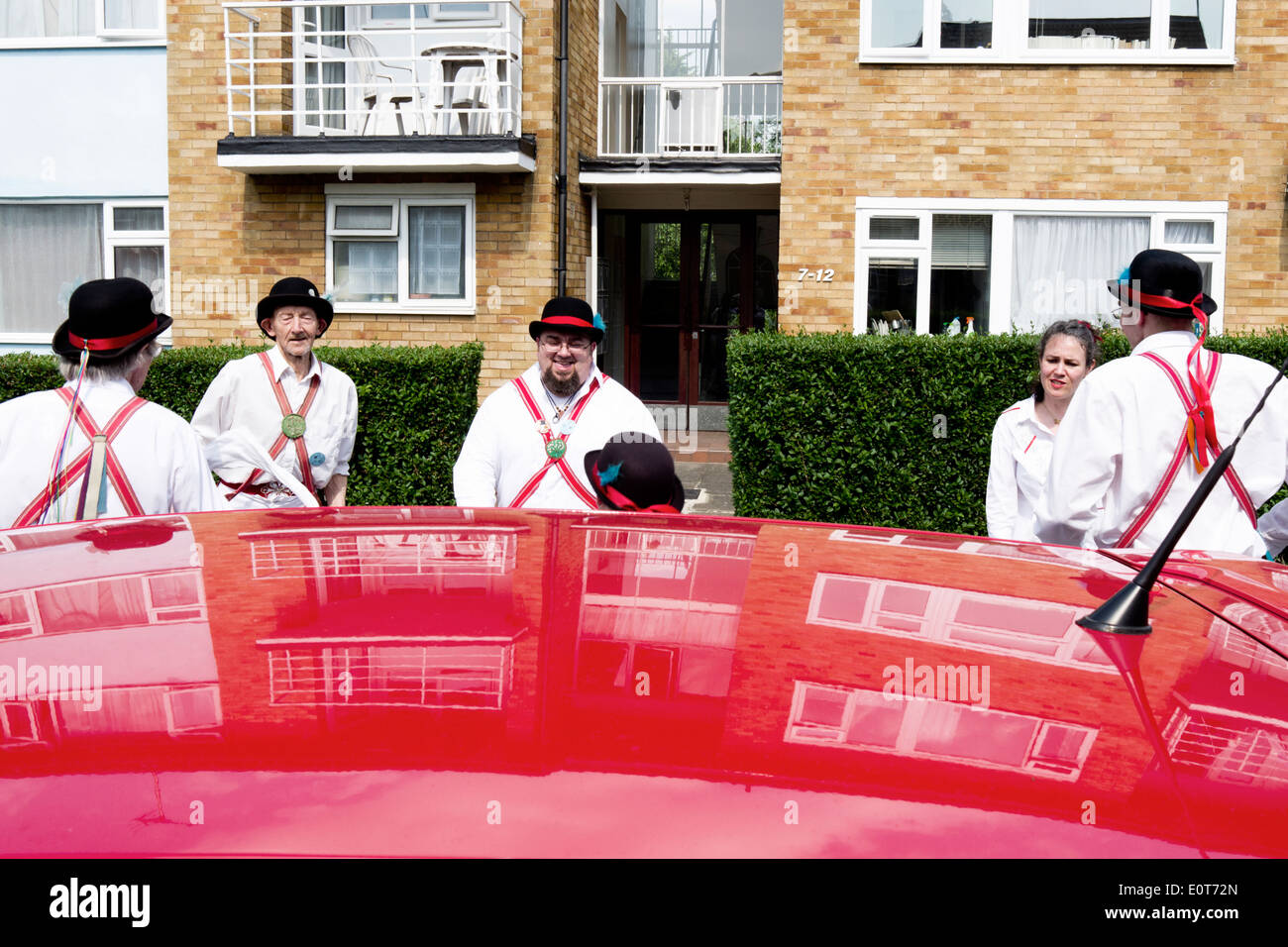 Morris Dancers vu de dessus le toit d'une voiture rouge, dans lequel les réflexions d'un bloc d'appartements est réfléchie. Banque D'Images