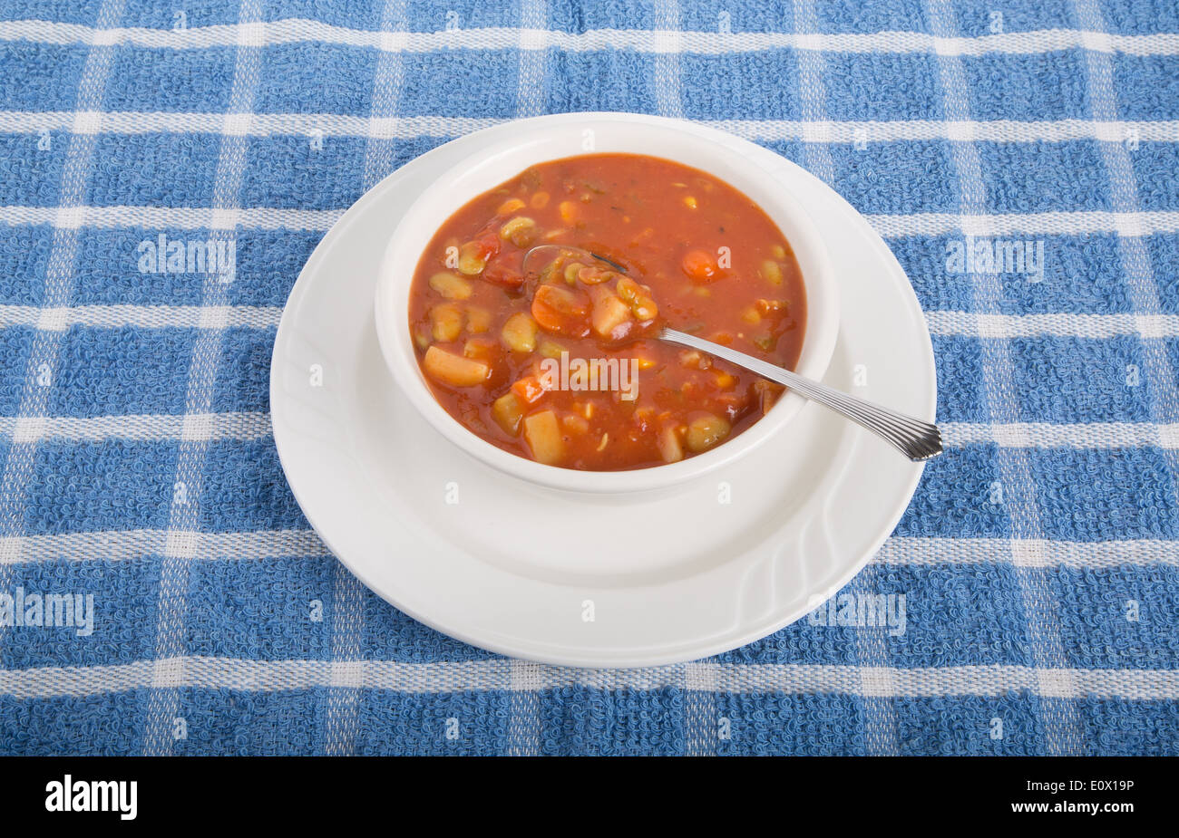 Un bol de soupe de légumes à base de tomates dans un bol blanc avec cuillère sur une serviette bleu Banque D'Images