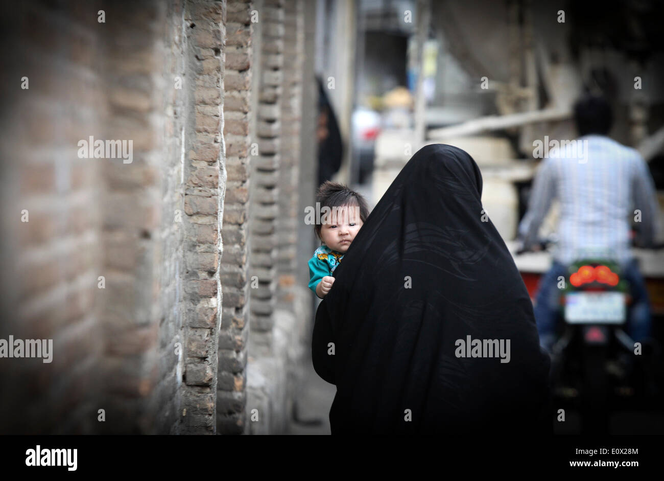 Téhéran, Iran. 19 mai, 2014. Une femme en tchador porte son enfant sur une ruelle à Téhéran, capitale de l'Iran, le 19 mai 2014. Tchador est un genre de Hijab officiel pour de nombreuses femmes en Iran dans les lieux publics. Le Hijab, une couverture des cheveux et le corps pour les femmes, a été tenu en public après la révolution islamique en Iran en 1979. © Ahmad Halabisaz/Xinhua/Alamy Live News Banque D'Images