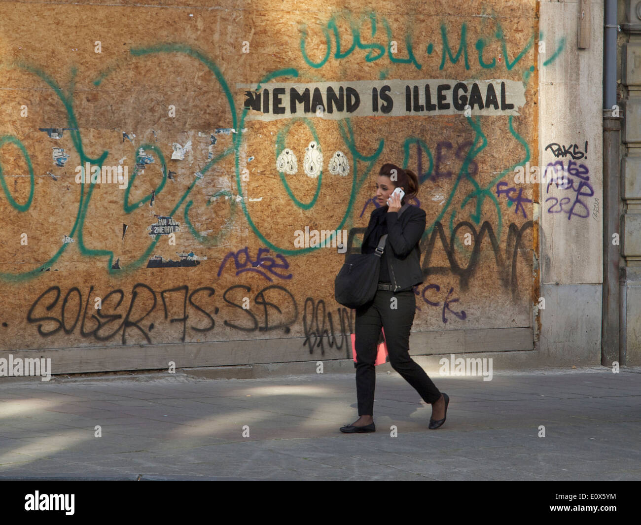 Woman talking on mobile phone avec graffiti disant personne n'est illégal en langue néerlandaise, Bruxelles, Belgique Banque D'Images