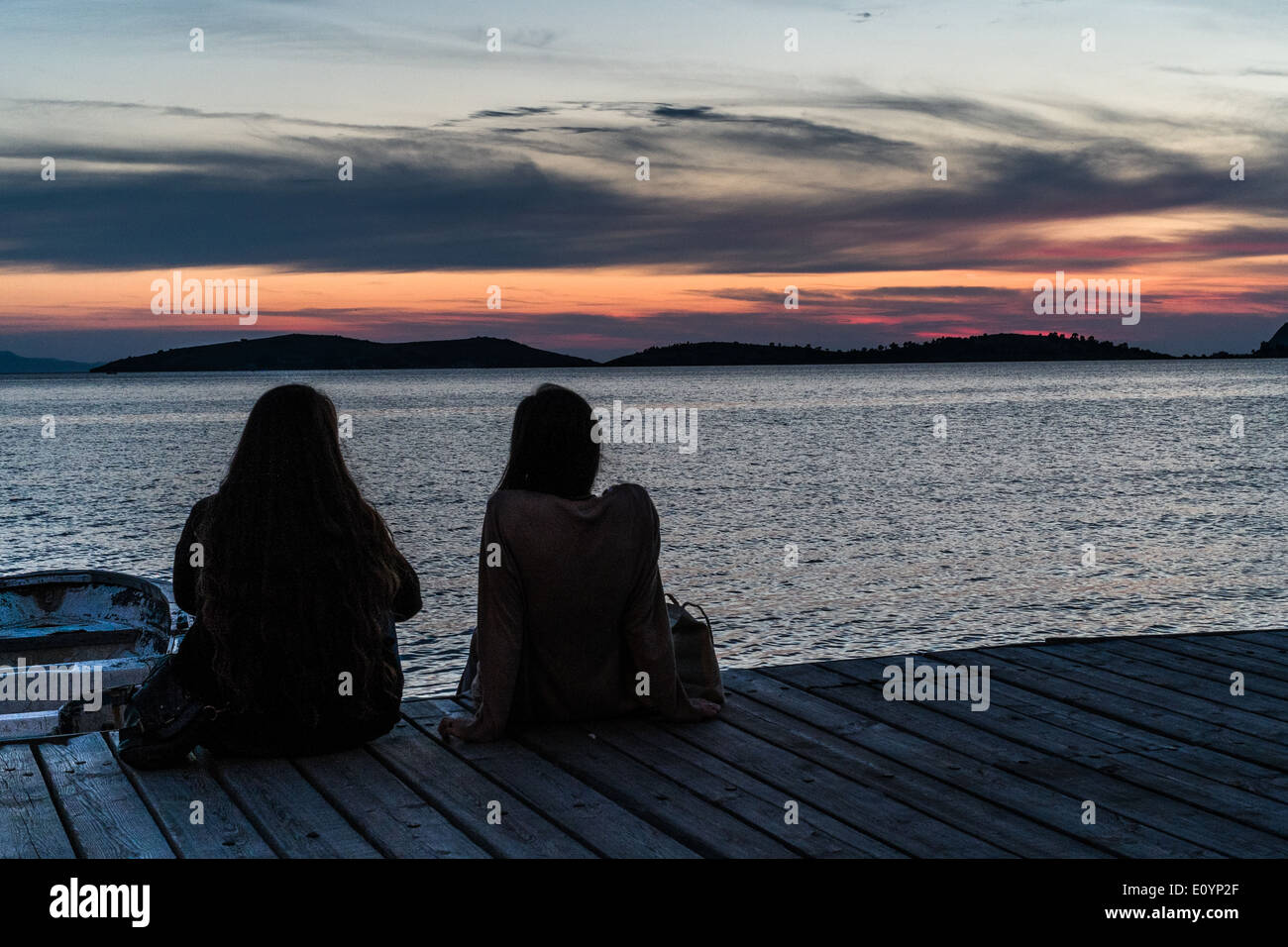 Coucher du soleil sur l'eau face à Foca, Izmir, Turquie District. Deux jeunes filles en silhouette assise sur le pontage. Banque D'Images