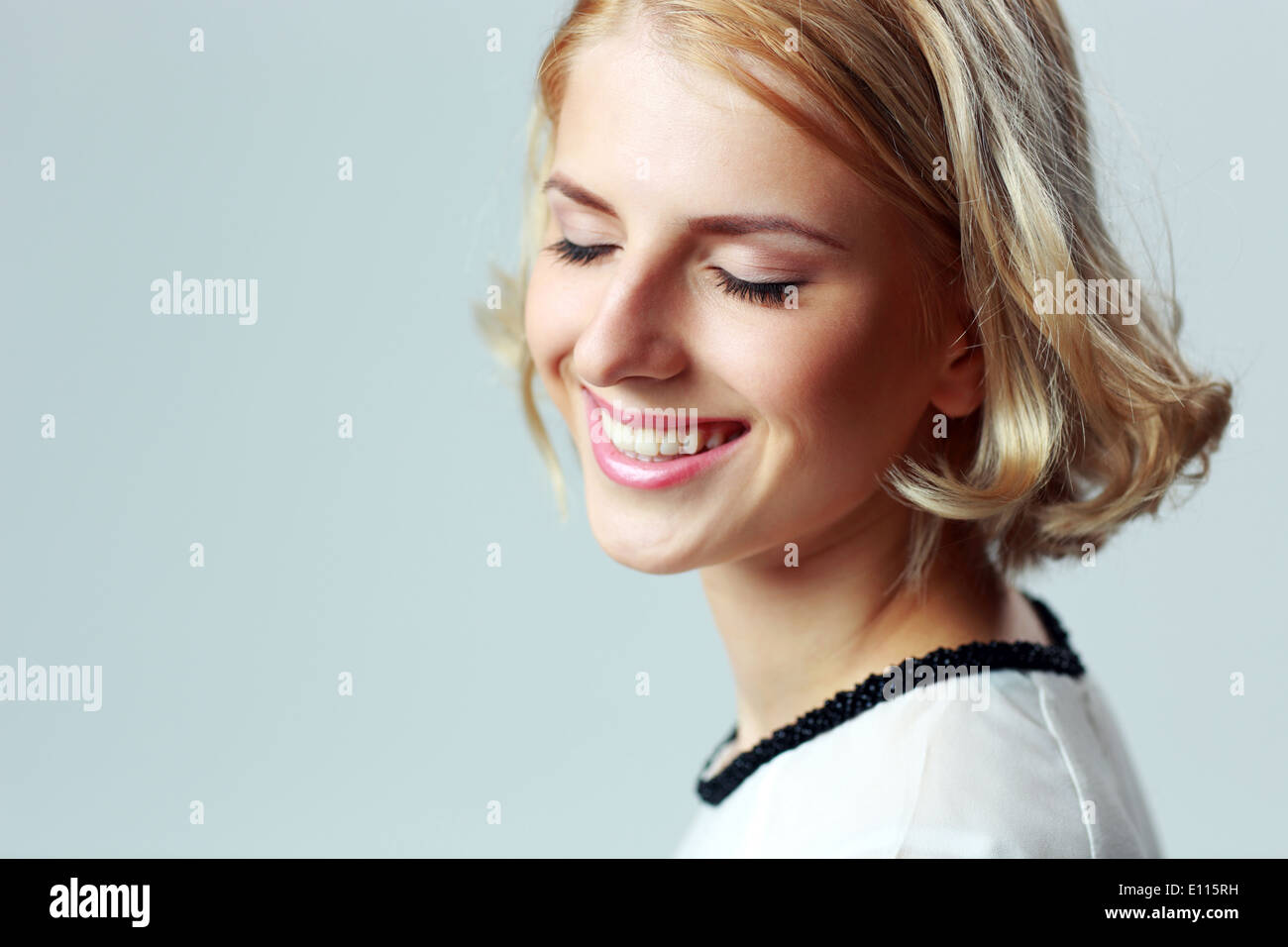 Closeup portrait of a smiling woman with closed eyes sur fond gris Banque D'Images