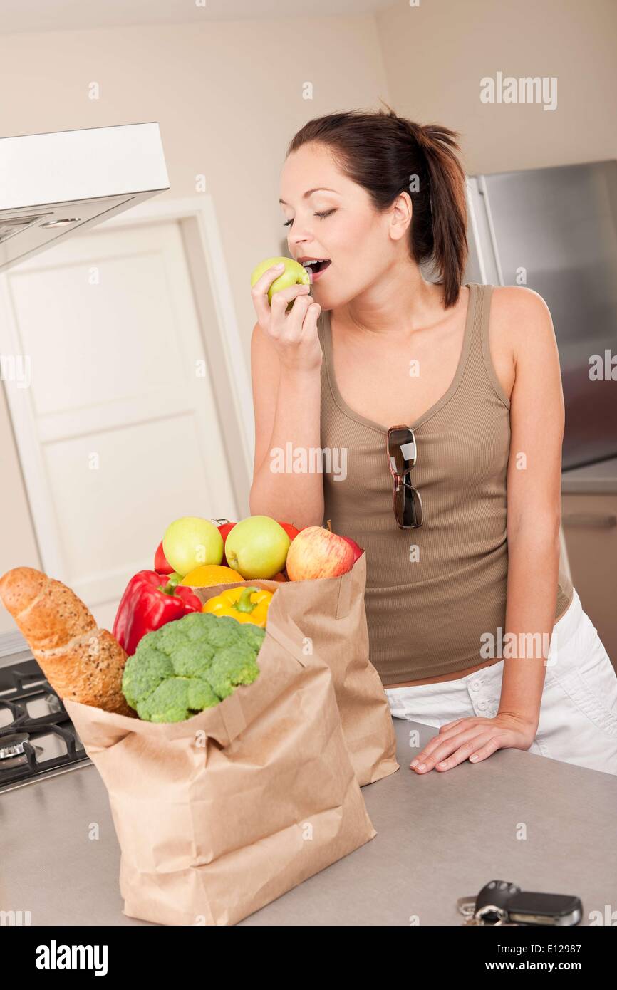 21 octobre 2009 - 21 octobre 2009 - jeune femme souriante avec des provisions dans la cuisine biting apple Banque D'Images