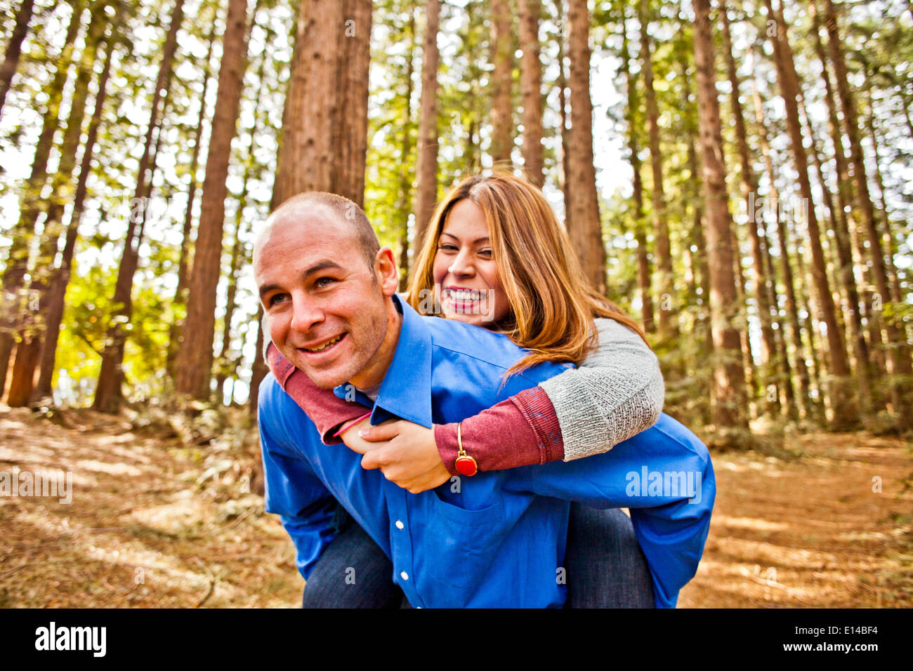 Hispanic man carrying girlfriend piggy back in forest Banque D'Images