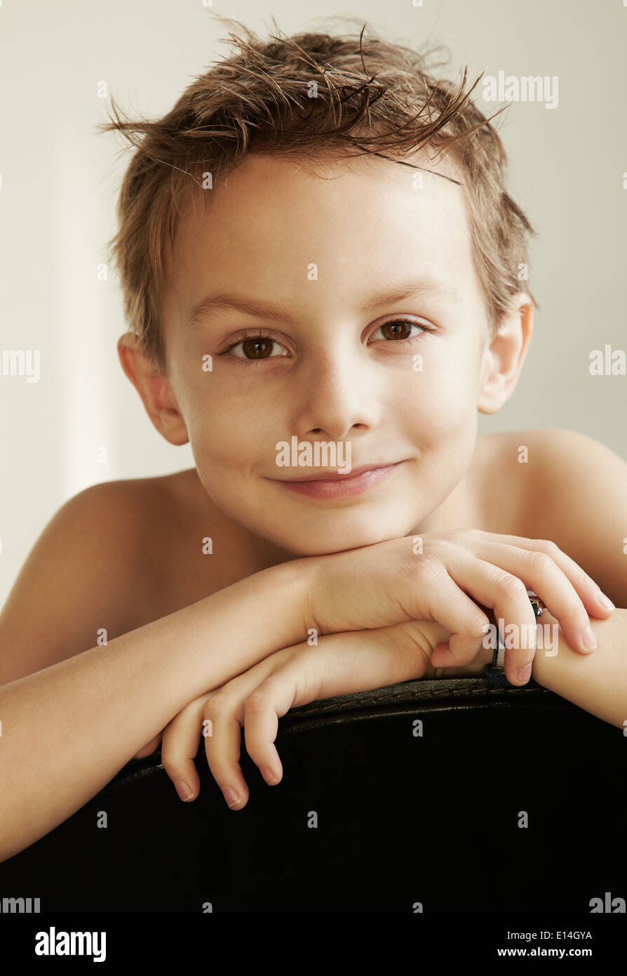 Portrait d'un jeune garçon de 7-8 ans reposant ses mains et de la tête sur le dos d'une chaise Banque D'Images