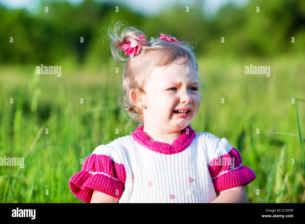 Adorable petit enfant fille pleurer sur l'herbe sur pré. La nature de fond vert d'été Banque D'Images