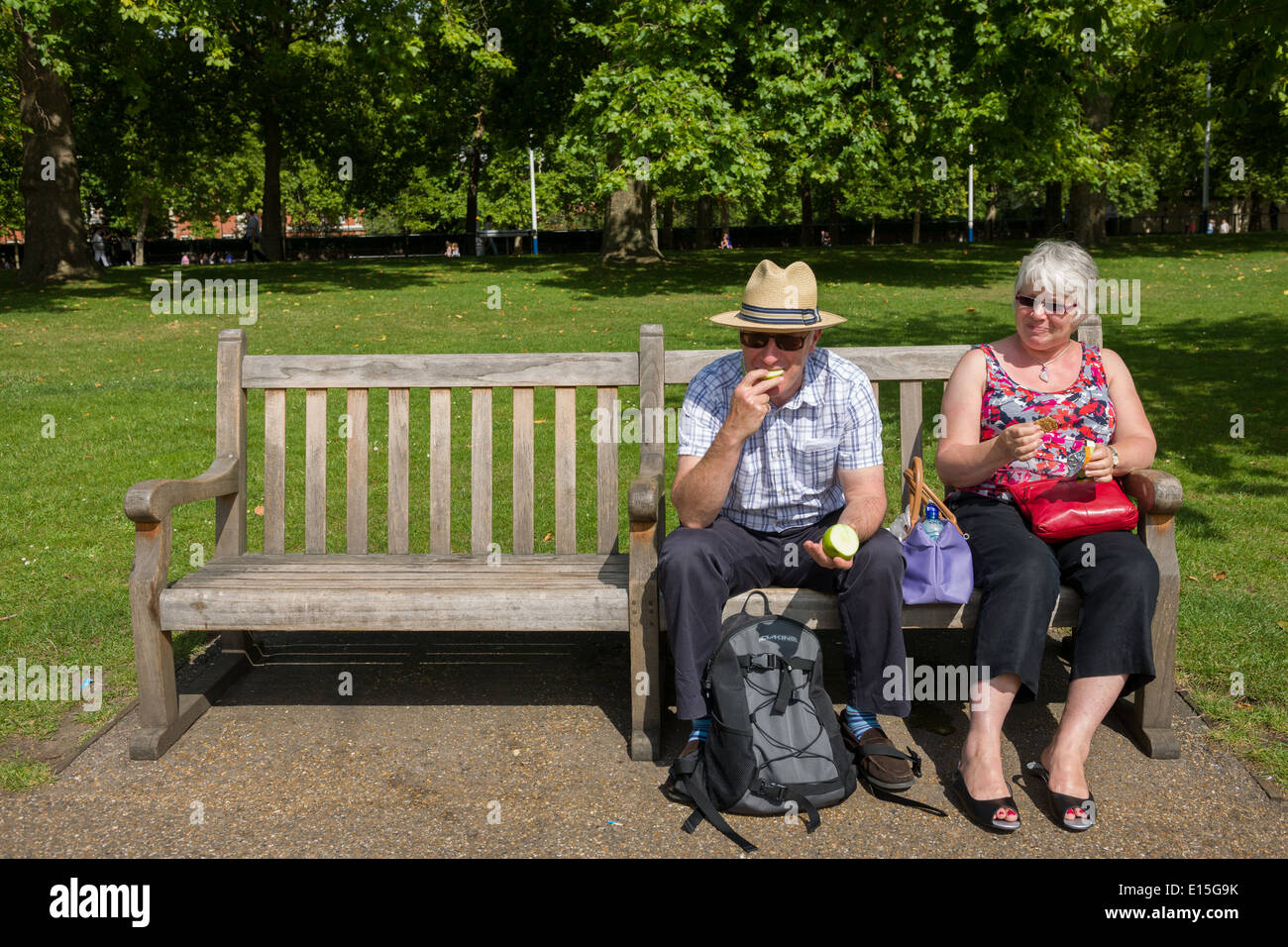 Couple d'âge moyen ayant un pique-nique sur un banc de parc, St James's Park, Londres, Angleterre Banque D'Images