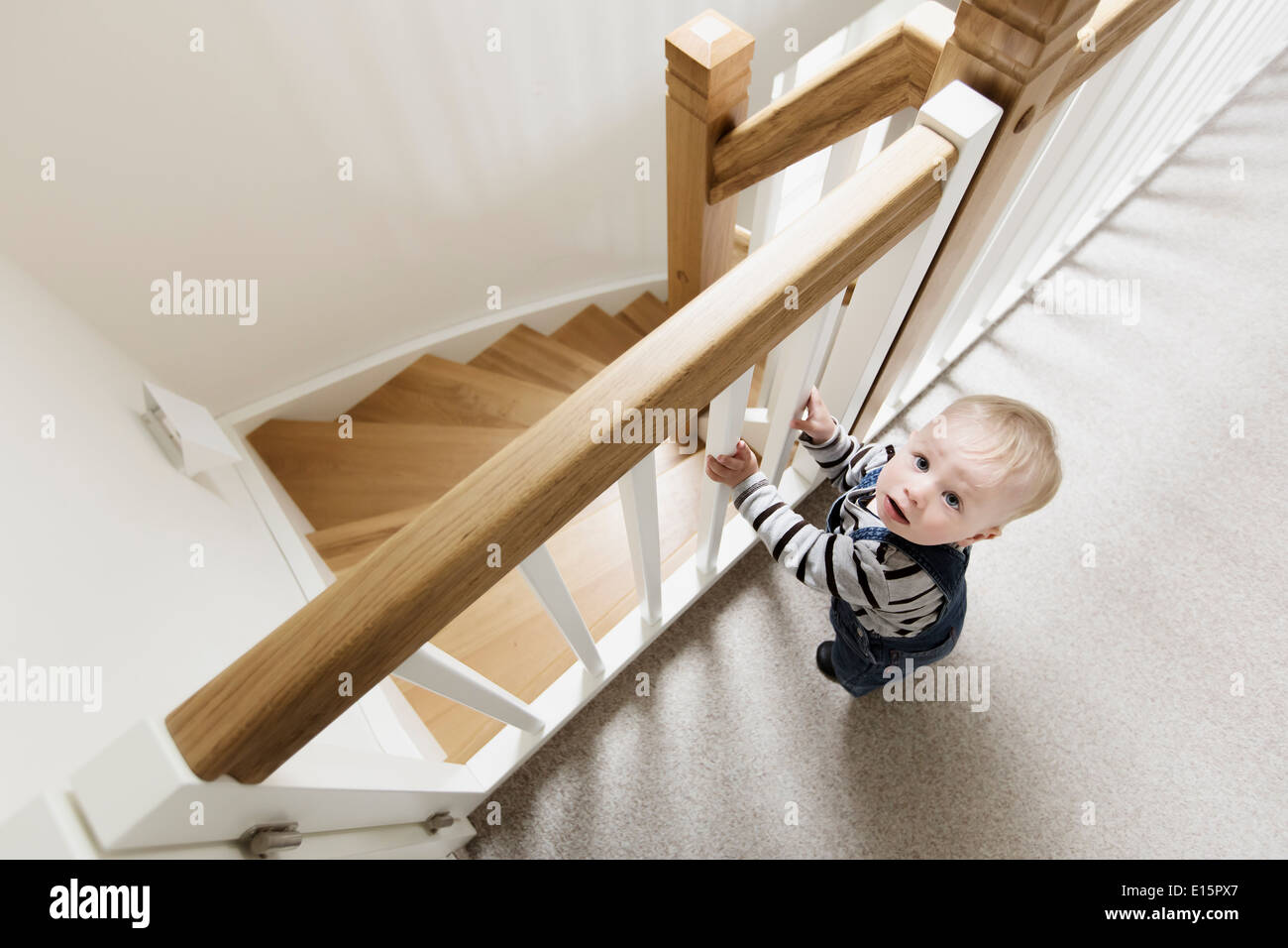 Bébé garçon, 1 ans, debout à la maison à un rail de protection fermé d'un escalier Banque D'Images