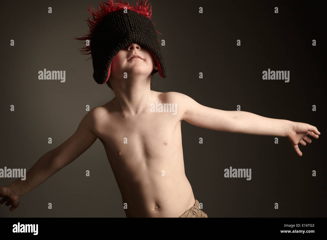 Garçon 4-5 ans avec un chapeau de ski noir et rouge mis sur l'arrière de manière qu'il a les yeux bandés mais semble curieux Banque D'Images