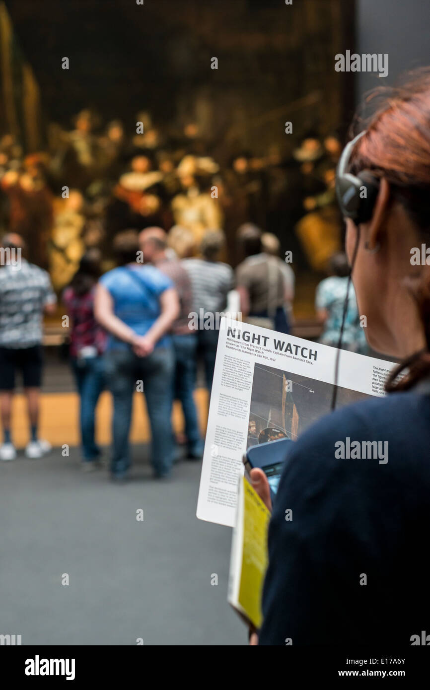 Femme de l'écoute d'un audio guide et de la lecture sur la Ronde de nuit de Rembrandt au Rijksmuseum, Amsterdam, Pays-Bas Banque D'Images