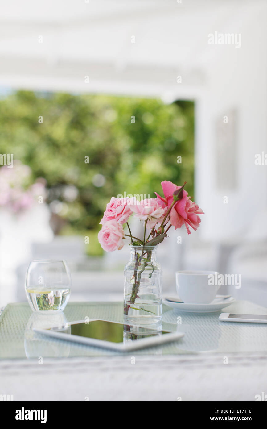 Roses rose sur table patio à côté de tasse à café et digital tablet Banque D'Images