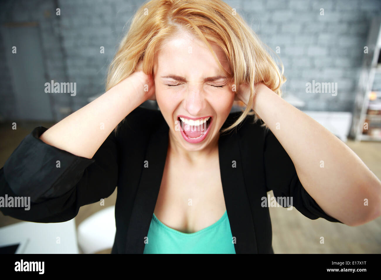Jeune femme criant avec les oreilles fermées in office Banque D'Images