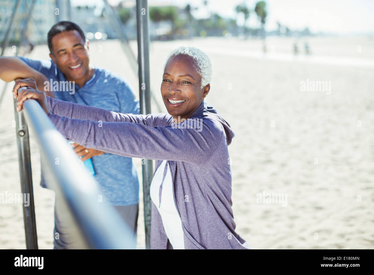 Portrait of senior couple leaning on bar à l'aire de jeux sur la plage Banque D'Images