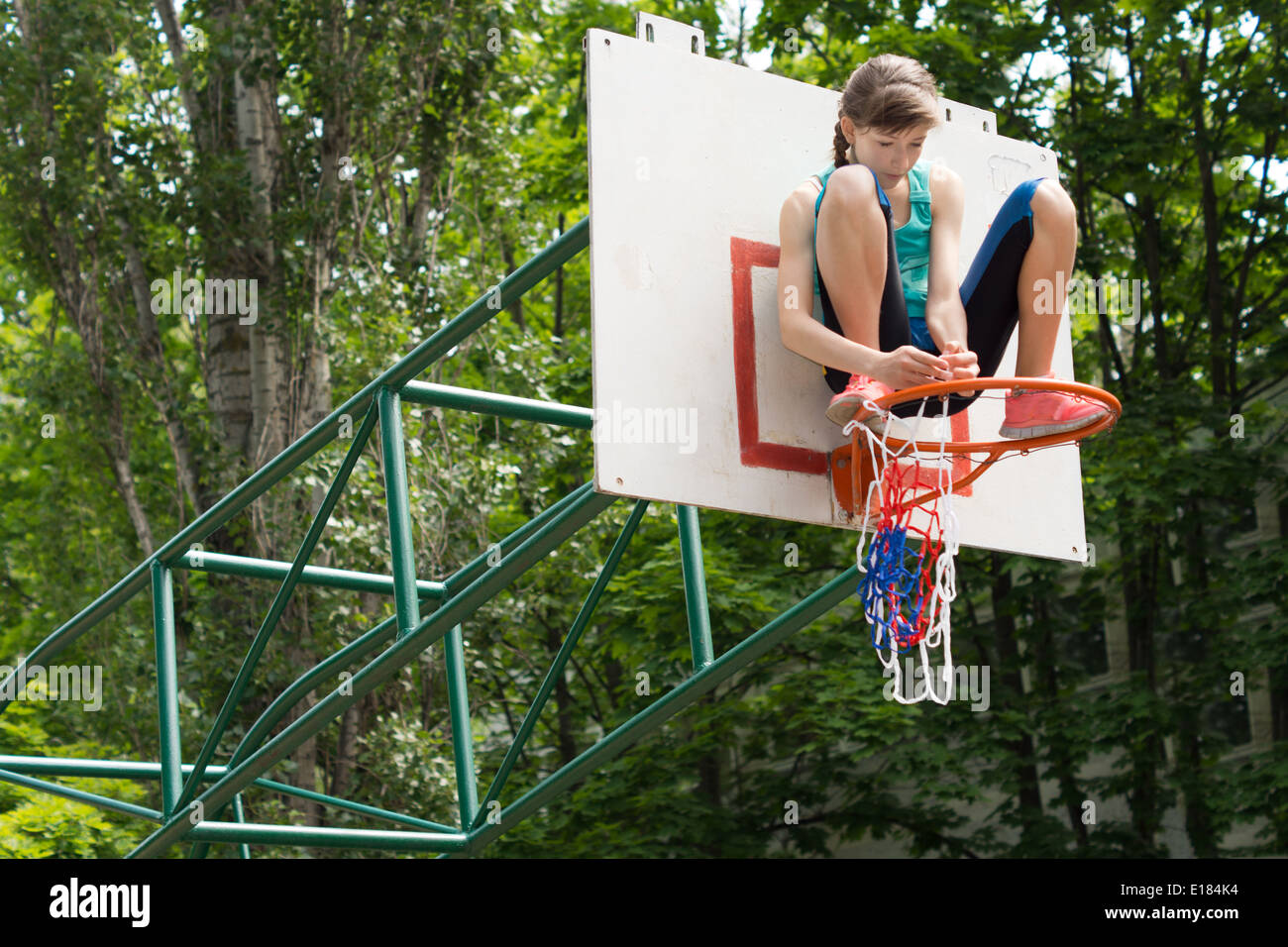 La fixation d'une jeune fille agile sur un terrain de basket-ball net Montant du but qui est posée sur le cercle de métal en le fixant avec ses mains Banque D'Images