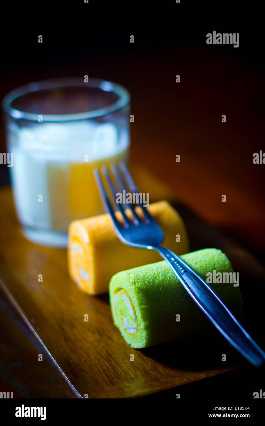 Deux "tranches" rouleaux Suisse orange vert jaune sur un bac ont une fourchette sur le dessus avec du lait dans le verre Banque D'Images