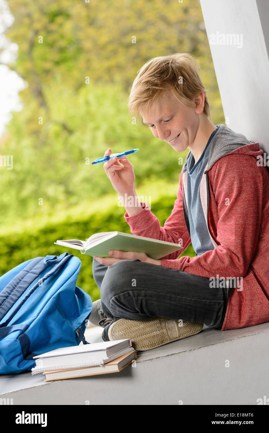 Smiling teenage boy sitting on wall en dehors de l'école Banque D'Images