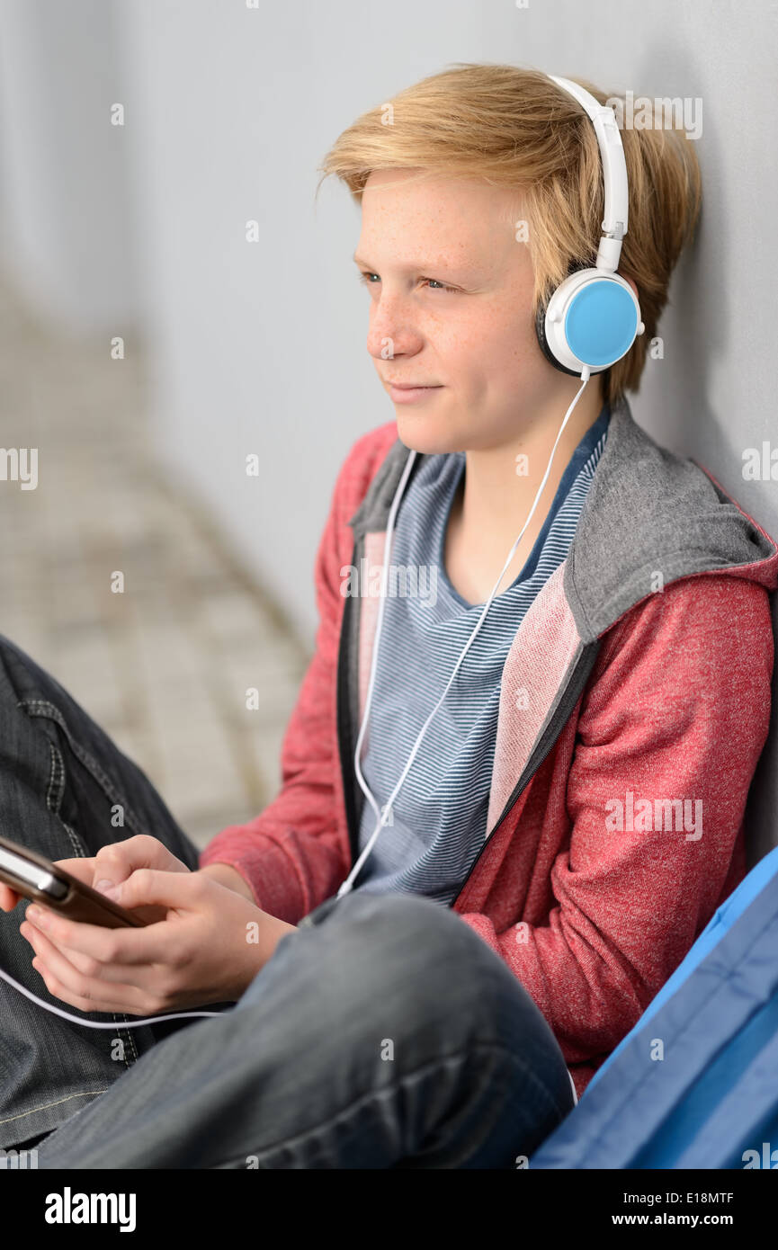 Teenage student réfléchie avec des écouteurs d'écouter de la musique assis dehors Banque D'Images