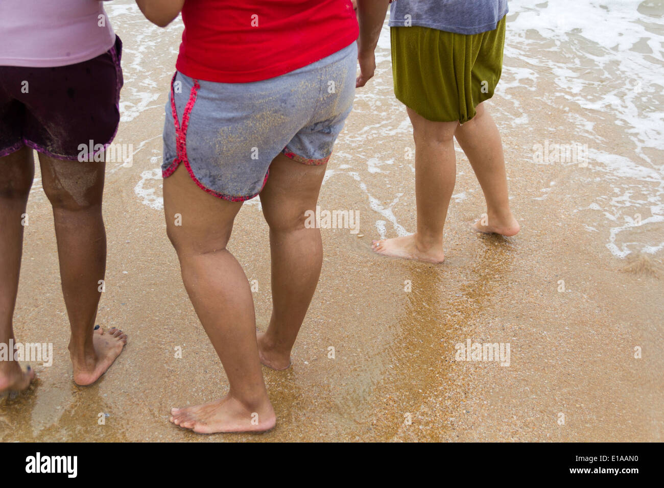 3 dames à une plage, en short, avec l'eau à quelques mètres de leurs pieds. L'eau s'estompe, et a laissé des traces Banque D'Images