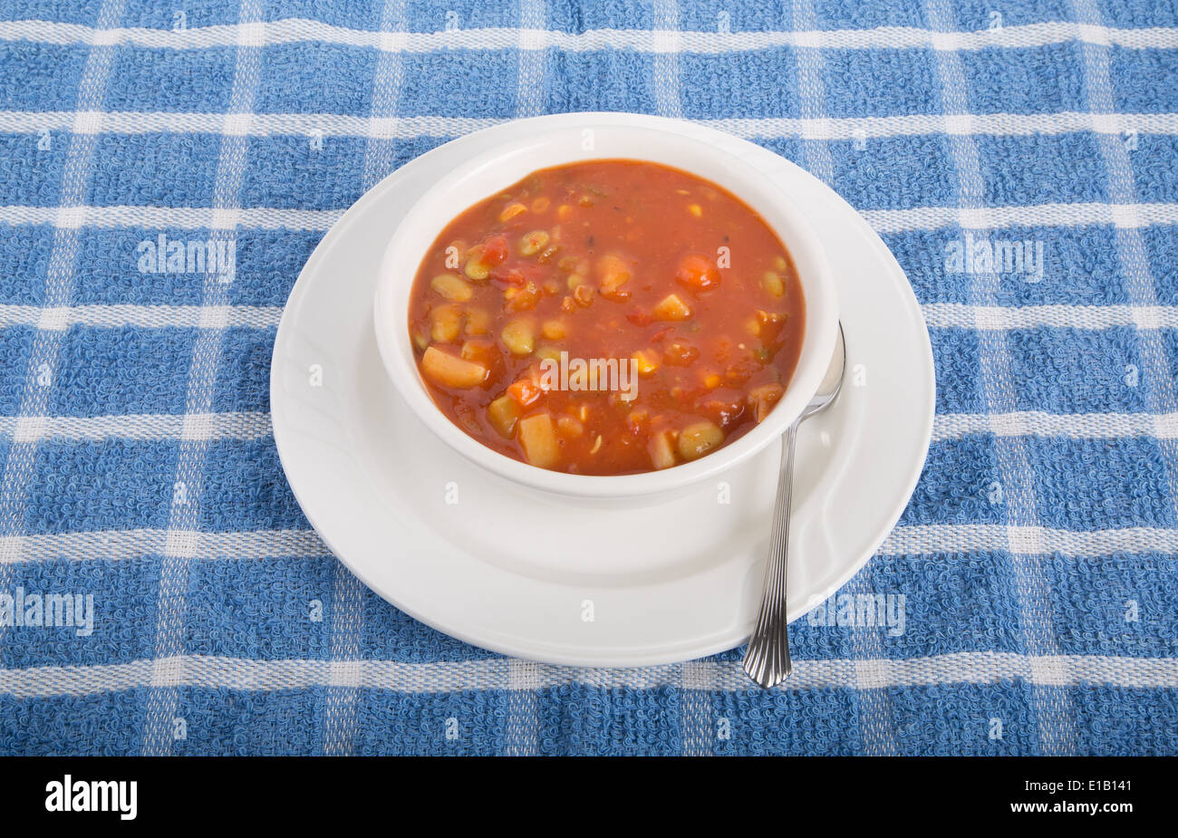 Un bol de soupe de légumes à base de tomates dans un bol blanc avec cuillère sur une serviette bleu Banque D'Images