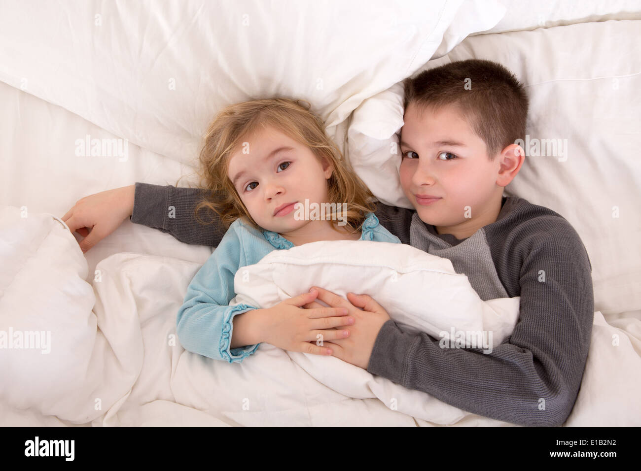 Affectueux petit frère et sœur au lit de câliner ensemble sous la couette jusqu'à la caméra à l'endormi Banque D'Images