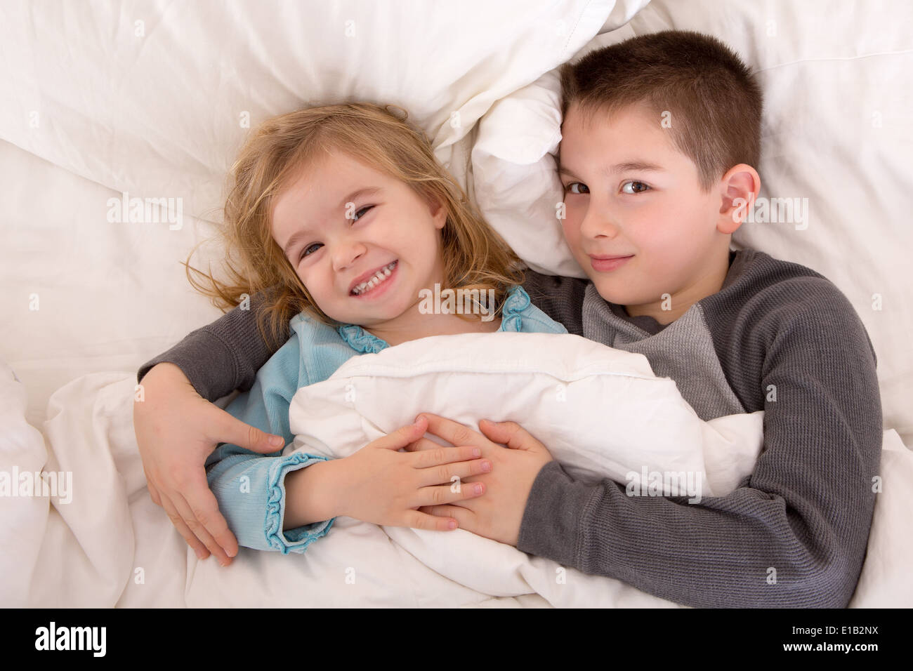 Les jeunes frère et sœur espiègle lit en souriant à la caméra en tant qu'elles se trouvent côte à côte sous la couette sommeil préparation Banque D'Images