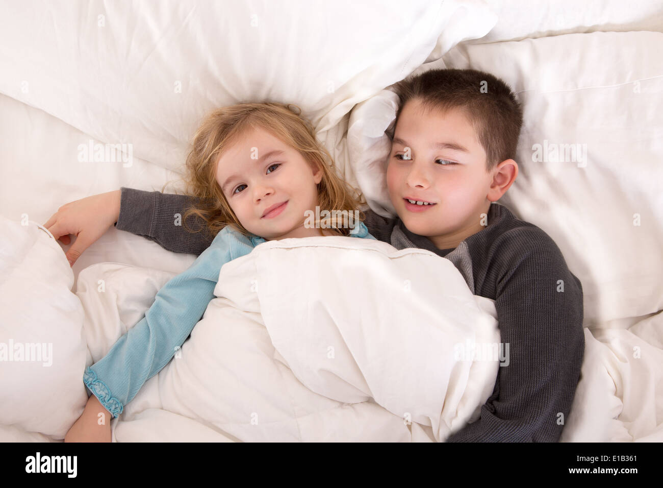 Jeune garçon de protection au lit avec sa petite sœur qui veille sur elle pendant qu'elle se trouve de l'appareil photo alors qu'ils préparent Banque D'Images