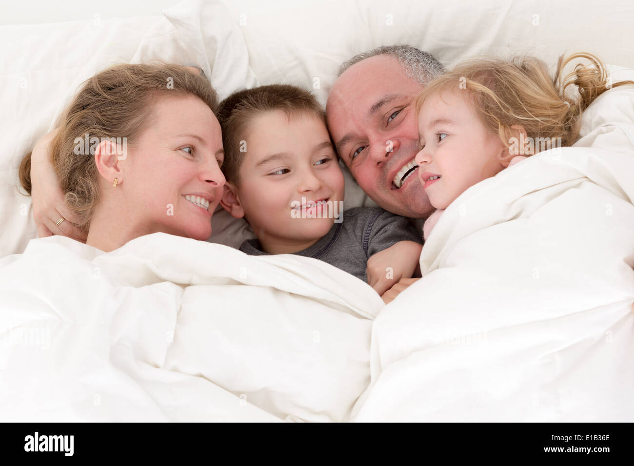 Heureux jeune famille câlins ensemble au lit avec une jolie jeune fille et son frère profitant de l'amour et de dévotion Banque D'Images