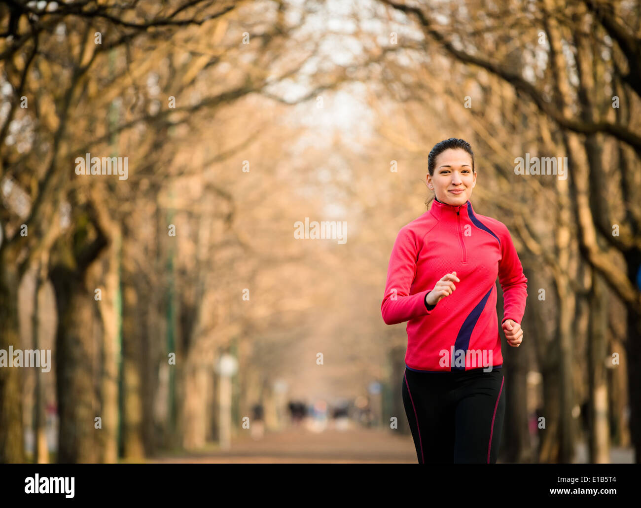 Jeune femme courir dans l'allée d'arbres - la fin de l'automne Banque D'Images