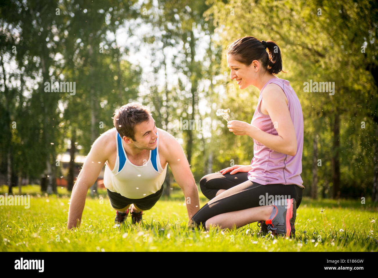 Man push-ups tout en femme souffle les graines de pissenlit sur lui - dans la nature en plein air Banque D'Images