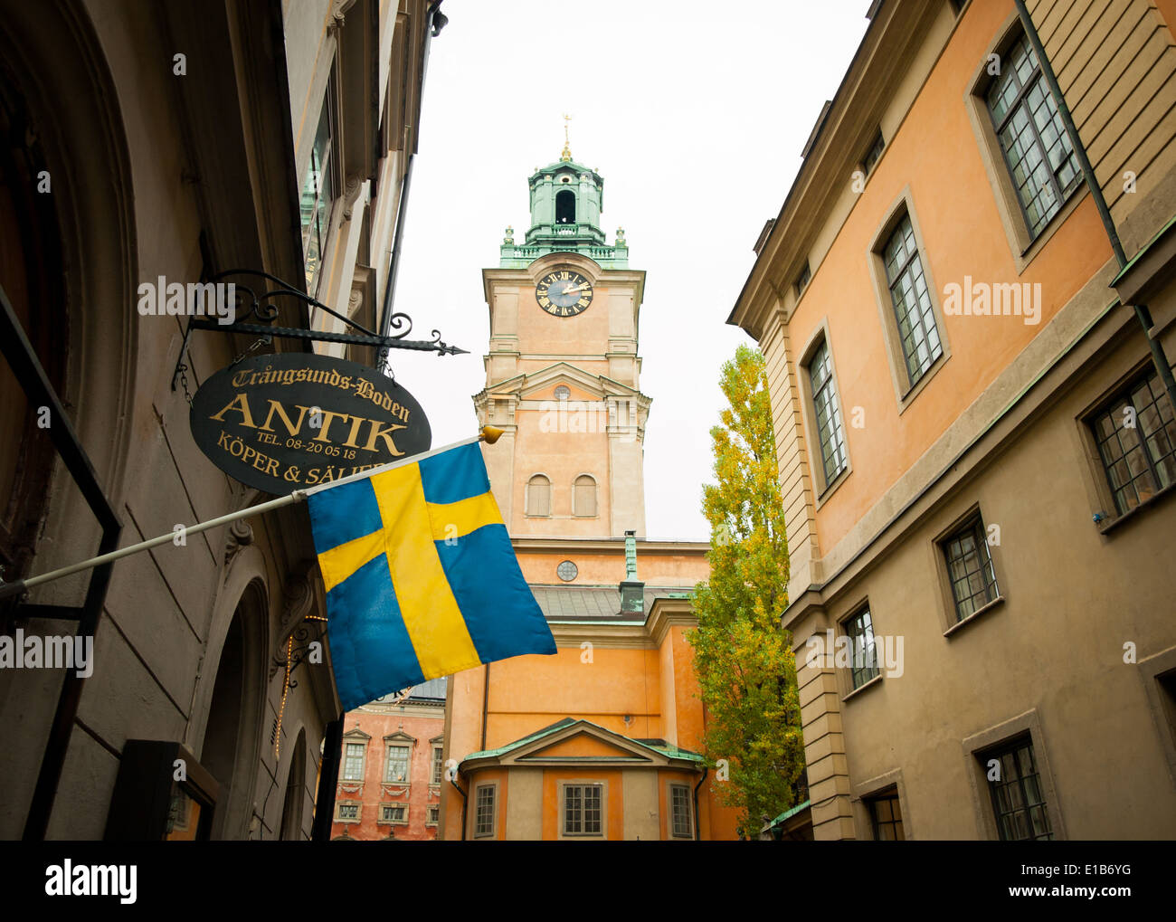 Un drapeau suédois est drapé devant un magasin sur Trångsund, comme la tour de l'horloge de Storkyrkan (la cathédrale de Stockholm), s'élève derrière. Banque D'Images