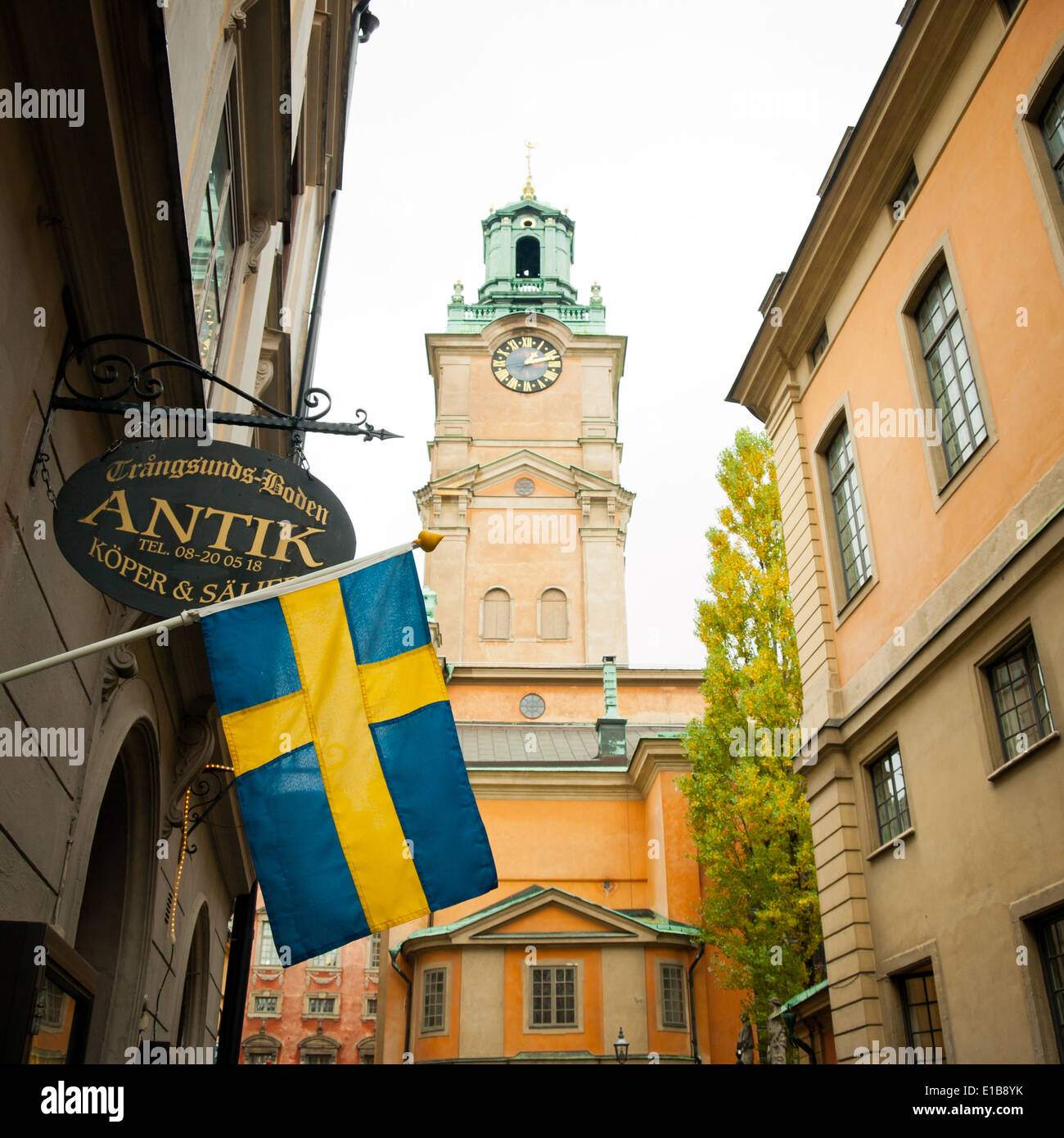 Un drapeau suédois est drapé devant un magasin sur Trångsund, comme la tour de l'horloge de Storkyrkan (la cathédrale de Stockholm), s'élève derrière. Banque D'Images