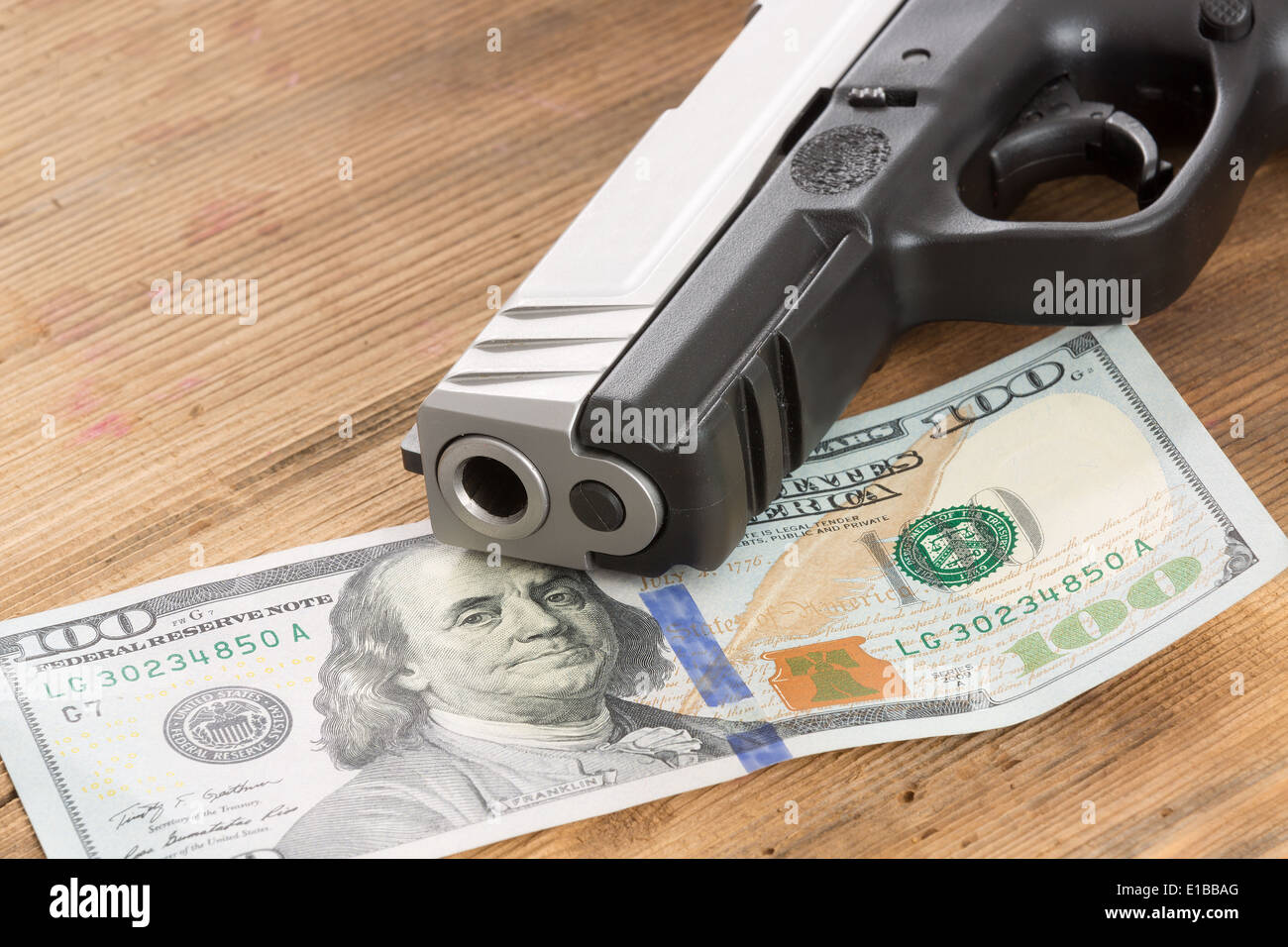 Close up de la bouche d'un pistolet avec un 100 American dollar bill allongé sur une table en bois dans une image conceptuelle de la criminalité, la corruption Banque D'Images
