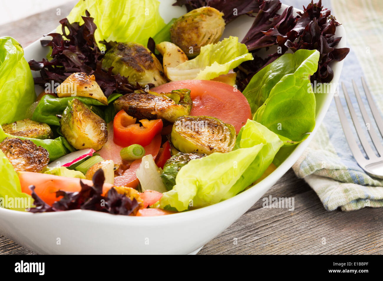 Bol de salade verte à feuilles en bonne santé avec les dés de tomates, choux de bruxelles sautés et radis servi dans un plat prêt pour un déli Banque D'Images
