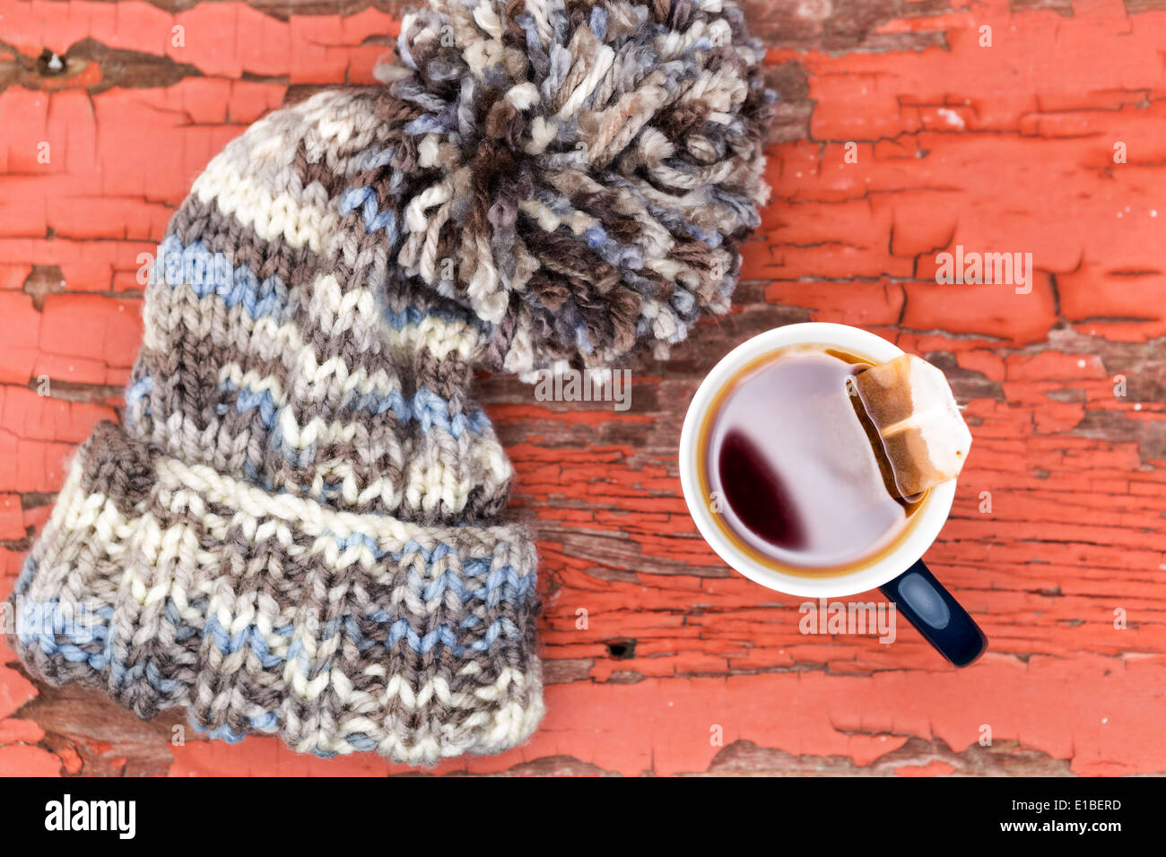 Vue de dessus d'un chapeau d'hiver laineux tricoté confortable avec un grand pompon à côté d'une tasse de thé chaud sur une surface en bois grunge Banque D'Images