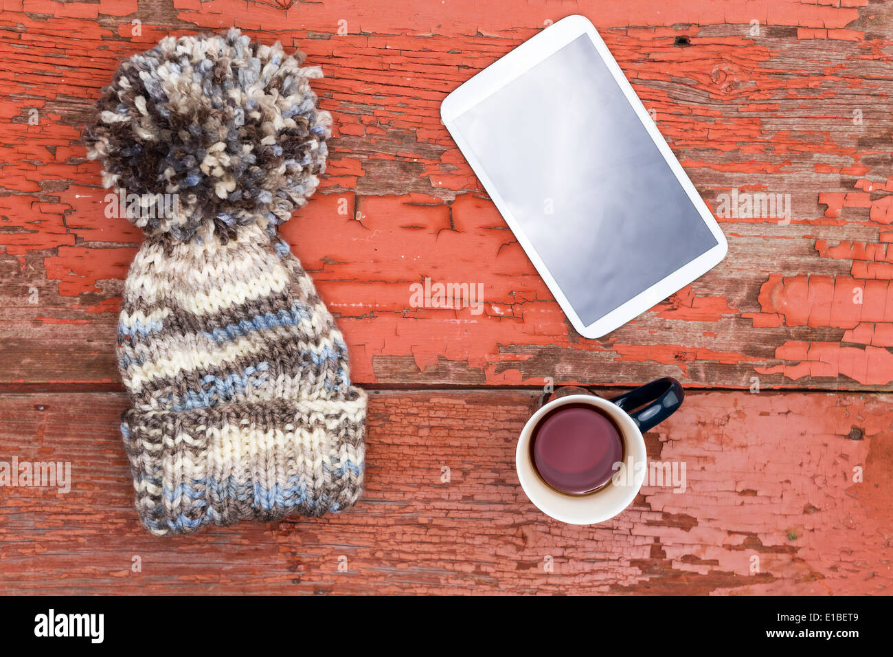 Chapeau hiver laineux avec un grand pompon décoratif couché avec une tablette et mug de thé sur une table en bois avec grunge Banque D'Images