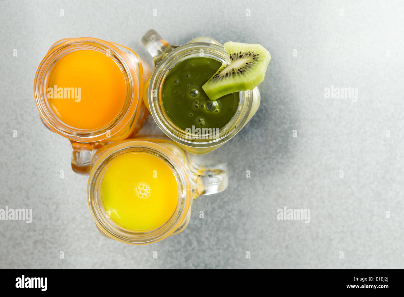 Vue de dessus de trois bouteilles de jus de fruits tropicaux frais y compris le jus d'orange, mangue jaune riche et un jus vert garni Banque D'Images