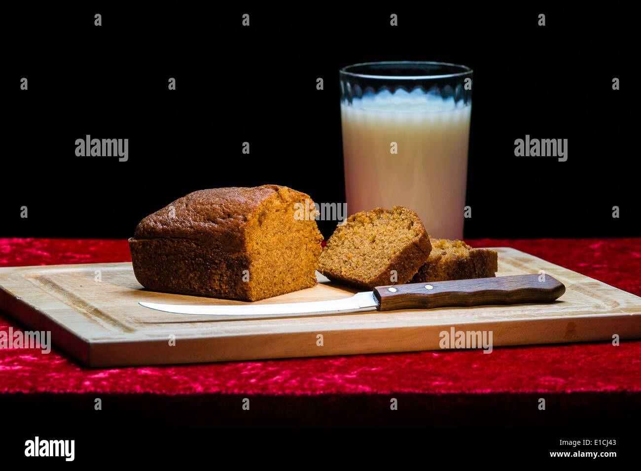 Pain à la citrouille, le couteau et le lait sur une planche à découper en bois, assis sur un tissu rouge sur fond noir Banque D'Images