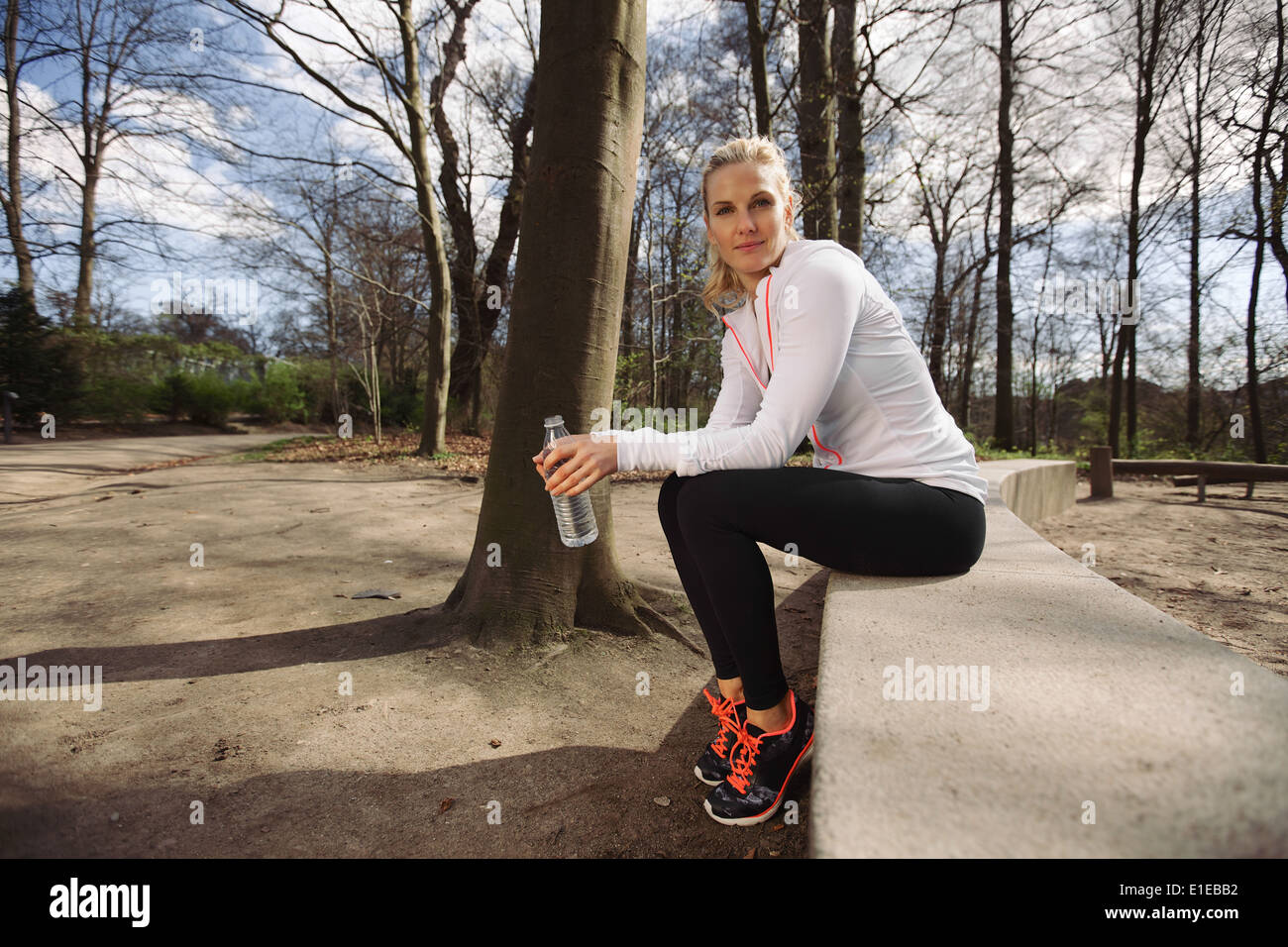 Coureuse en faisant une pause de courir dans la forêt. Belles jeunes femmes athlètes assis avec une bouteille d'eau. Banque D'Images