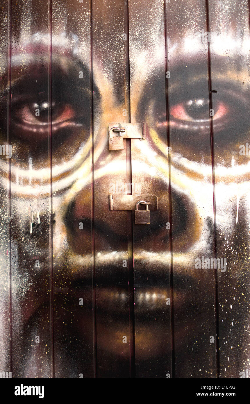 Les graffitis de rue d'un visage d'enfant dans une tribu composent, peint sur le devant d'une porte en bois cadenassée. Banque D'Images