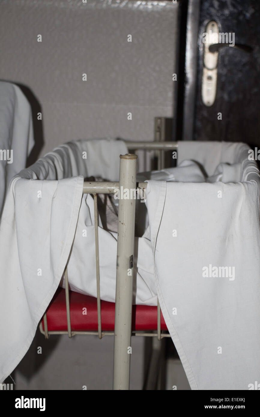 Un lit métallique destiné à l'intérieur d'une chambre d'hôpital de bébés, couvert par un drap blanc. Il dispose d'un coussin rouge et avec des couvertures sur le dessus Banque D'Images