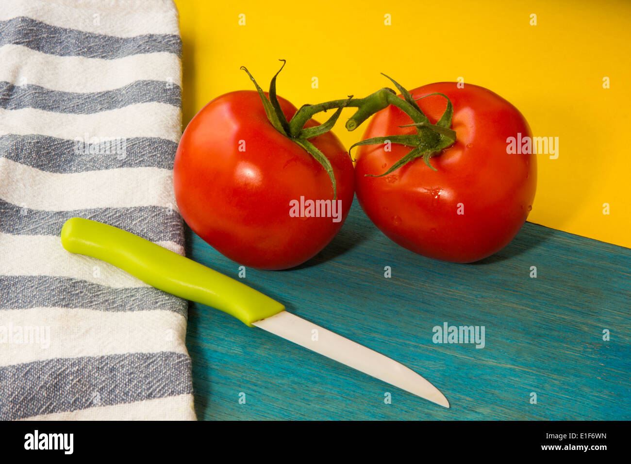 Image colorée montrant deux tomates rouges, un couteau et un fond bleu et jaune. Banque D'Images